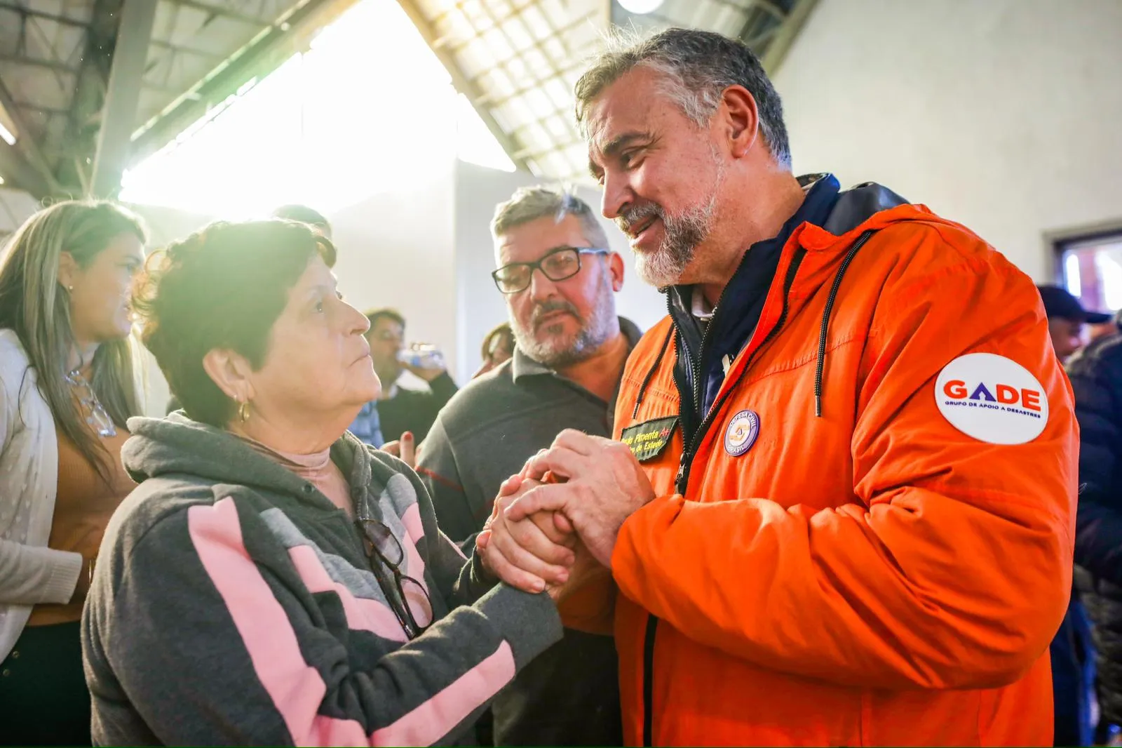 Paulo Pimenta, de casaco da Defesa Civil, segura as mãos de uma moradora atingida pela enchente de 2024